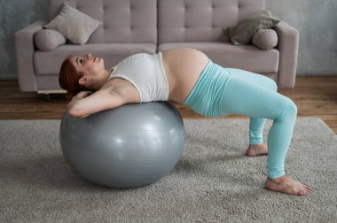 Hamile kızıl saçlı kadın evde fitball ile kol egzersizi yapıyor.