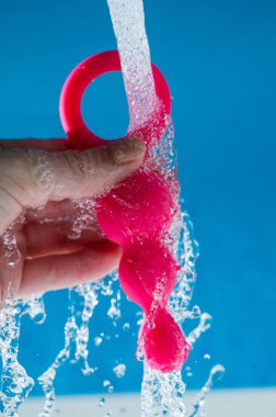 Mavi arka planda akan suyun altında pembe anal boncuklar tutan bir kadın. Seks oyuncağı hijyen konsepti