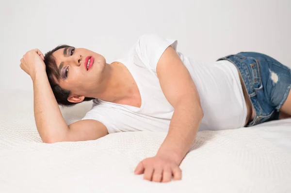Caucasian transgender man lies on bed. Gay posing in the bedroom