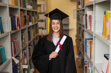 Mezuniyet elbisesi içinde, elinde diploması olan mutlu genç bir kadın.