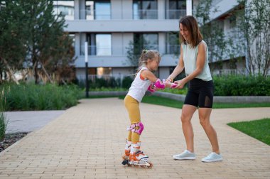 Anne kızının paten kaymasını öğrenmesine yardım ediyor.