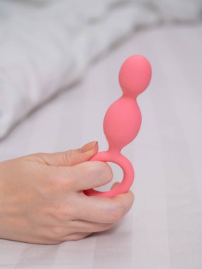 Yatakta uzanmış pembe anal boncuklu bir kadının yakın çekimi.