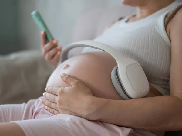 妊娠中の女性がスマートフォンで子供のために音楽を聴く 腫瘍のヘッドフォン — ストック写真