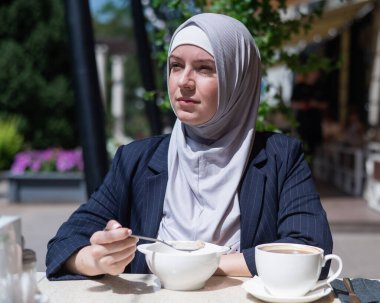 Beyaz kadın tesettürlü, açık kafede kahvaltı yapıyor.