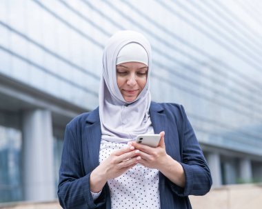 Açık havada akıllı telefon kullanan tesettürlü ve takım elbiseli bir iş kadını