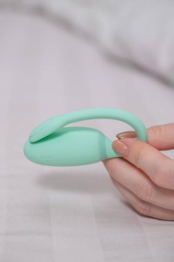 Beyaz çarşafta uzanırken elinde naneli vibratör tutan kadın.