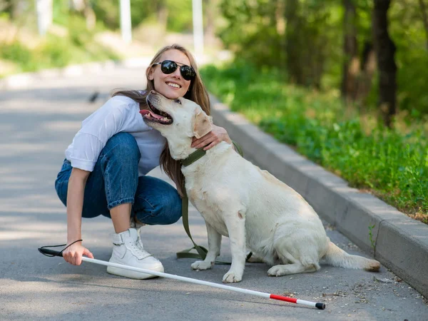Blind young woman cuddling with guide dog on a walk outdoors