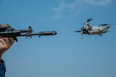 Bir adam mavi gökyüzüne karşı uçan bir drona ateş etmeyi hedefliyor.