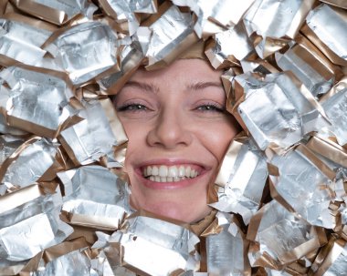 The face of a Caucasian woman surrounded by candy wrappers