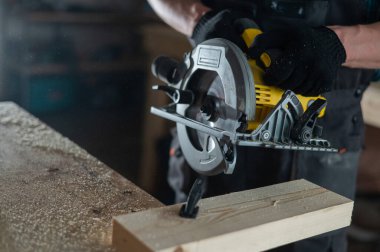 Usta atölyede dairesel bir testere ile tahtayı keser. Bir marangozun elleri iş başında.