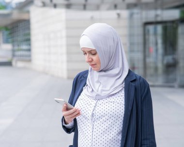 Açık havada akıllı telefon kullanan tesettürlü ve takım elbiseli bir iş kadını