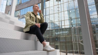 İşitme cihazı olan düşünceli beyaz adam şehir merkezindeki merdivenlerde oturuyor.