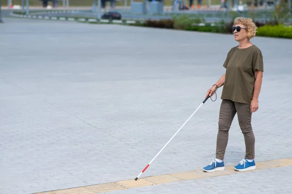 一位年老的失明妇女带着手杖沿着一块触觉瓷砖行走 — 图库照片