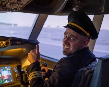 Uçuş simülatörü kullanırken gülümseyen beyaz sakallı bir adam. Pilot kokpitte baş parmak gösteriyor.