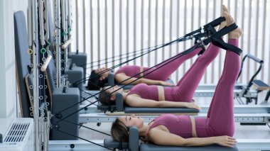 Pembe spor kıyafetli üç Asyalı kadın ıslah yatağıyla pilates egzersizi yapıyor.