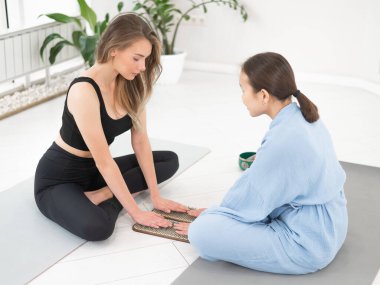 İki kadın elleri sadhu tahtalarında yoga minderlerinde oturuyor.