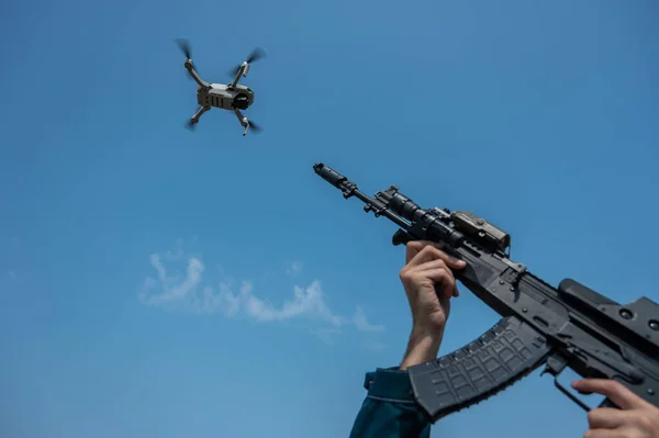 A man aims to shoot a rifle at a flying drone against a blue sky