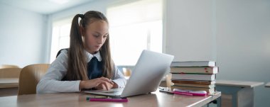 Beyaz kız sınıfta dizüstü bilgisayarla ders çalışıyor.