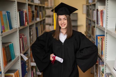 Mezuniyet elbisesi içinde, elinde diploması olan mutlu genç bir kadın.