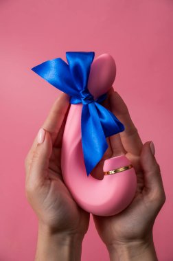 Woman holding curved dildo with blue ribbon on pink background