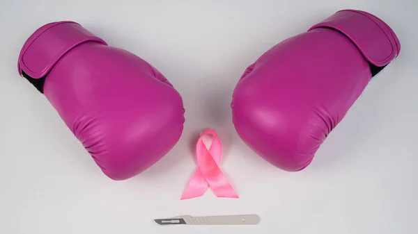 Pink boxing gloves, a surgical scalpel and a pink ribbon on a white background. The concept of fighting breast cancer