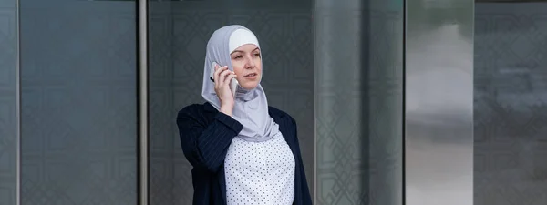 Business woman in hijab and suit talking on smartphone while leaving the business center