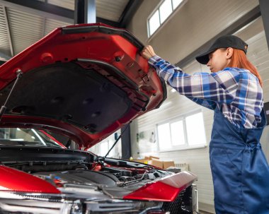 Kadın oto tamircisi araba servisinde bir arabanın kaputunu açıyor.
