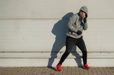 Kapüşonlu bir adam gri bir duvara karşı boks antrenmanı yapıyor.