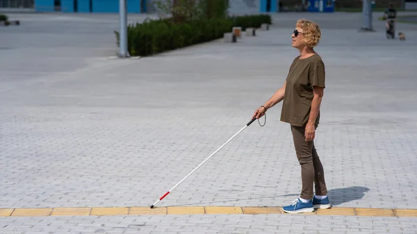一位年老的失明妇女带着手杖沿着一块触觉瓷砖行走 — 图库照片