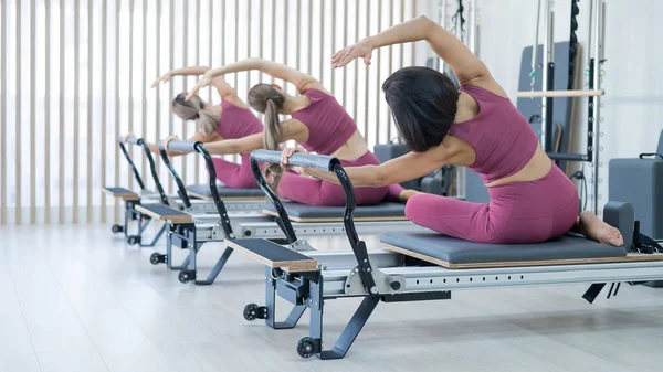 Three Asian Women Pink Sportswear Doing Side Bends Reformer Machine — Stockfoto