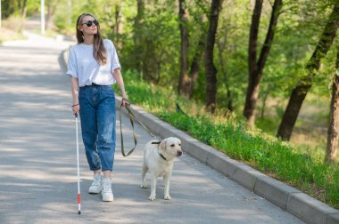 Kör kadın parkta rehber köpekle yürüyor.