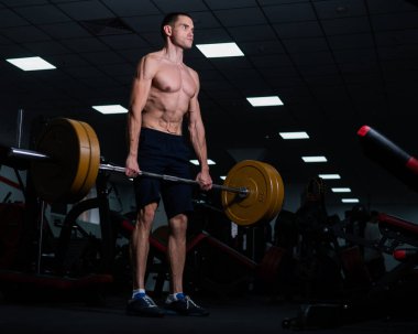 Shirtless man doing bicep exercises with dumbbells in the gym