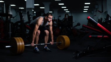 Salonda dambıllarla pazı egzersizi yapan bir adam.