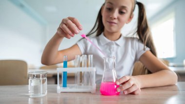 Liseli bir kız kimya dersinde deneyler yapıyor. Beher kabından renkli sıvılar döken bir kız.