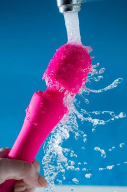 Bir kadın mavi arka planda akan suyun altında pembe bir vibratörü yıkıyor. Seks oyuncağı hijyen konsepti