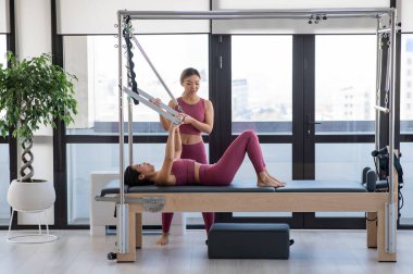 Cadillac reformcusu eğitmeniyle pilates yapan Asyalı kadın.