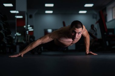 Spor salonunda şınav çeken kaslı üstsüz bir adam.