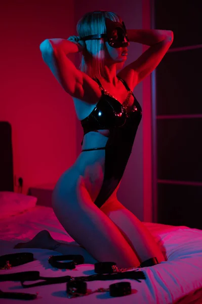 性感的金发女人 戴着皮革面具 身穿紧身衣 穿着深蓝色霓虹灯 躺在卧室里 角色扮演游戏 — 图库照片