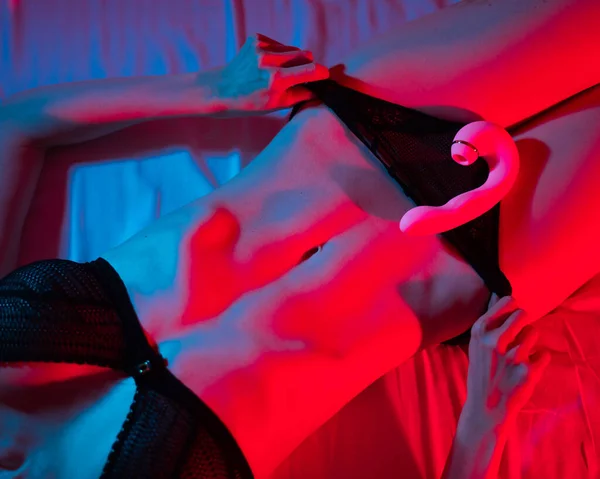 stock image A faceless woman lies in a bedroom in a blue-red neon light and uses a pink vibrator. Close-up of the abdomen