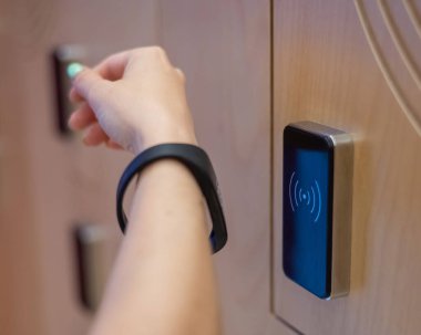 Bir kadın soyunma odasındaki kabinin elektronik kilidini bileziğiyle açıyor.