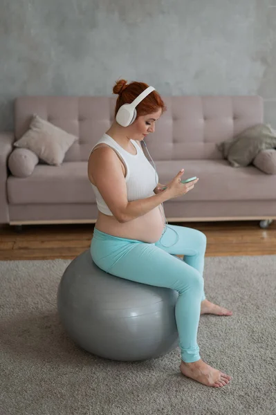Caucásico Pelirrojo Embarazada Sentada Fitball Escuchando Música Con Auriculares Casa —  Fotos de Stock