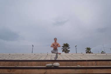 Beyaz bir adam, çıplak gövdesiyle deniz kıyısında wushu yapıyor.