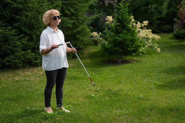 An elderly blind woman lays out a tactile cane while walking in the park