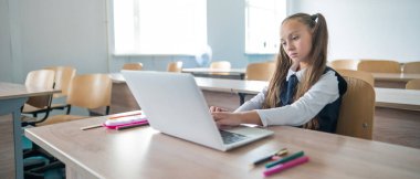 Beyaz kız sınıfta dizüstü bilgisayarla ders çalışıyor.