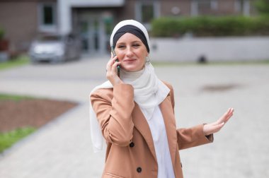 Açık havada akıllı telefondan konuşan tesettürlü genç kadın.