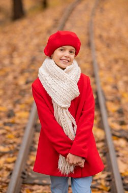 Kırmızılı ve bereli beyaz kız sonbaharda parkta tren yolu boyunca yürür.