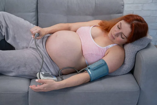 Hamile Bir Kadın Kanepede Yatarken Kan Basıncını Bir Tonometreyle Ölçer — Stok fotoğraf