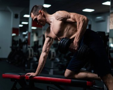 Gömleksiz bir adam spor salonunda dambıl sırasına dizer.