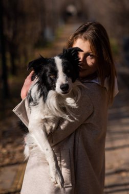 Sonbahar parkında yürürken kollarında bir çoban köpeği tutan beyaz kadın. Köpekli bir kızın portresi.