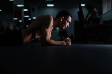 Spor salonunda dirsek tahtası yapan kaslı üstsüz bir adam.